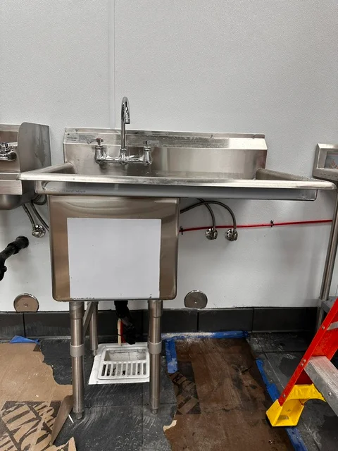 Commercial stainless steel sink with faucet mounted on steel stand in workshop