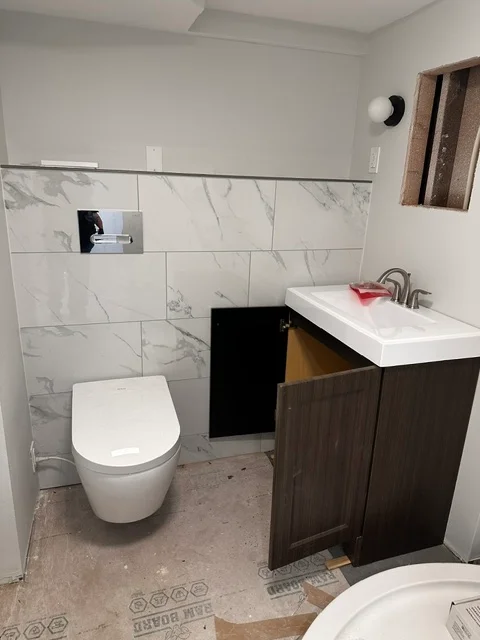 Modern bathroom with marble tile walls, dark wood vanity, white toilet, and chrome fixtures