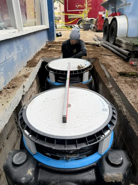 Technician installing dual septic tanks in underground trench next to residential building