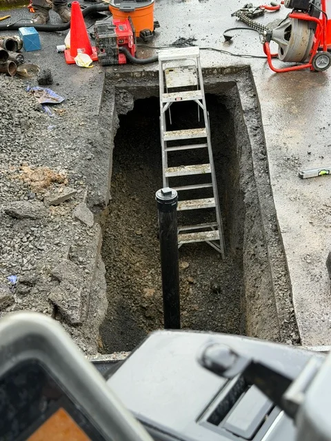 Excavated sewer line trench with ladder access and underground piping visible