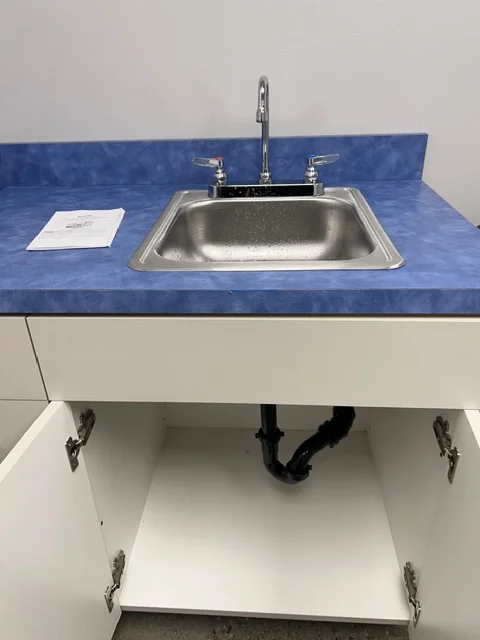 Stainless steel kitchen sink with chrome faucet installed on blue countertop with white cabinet base