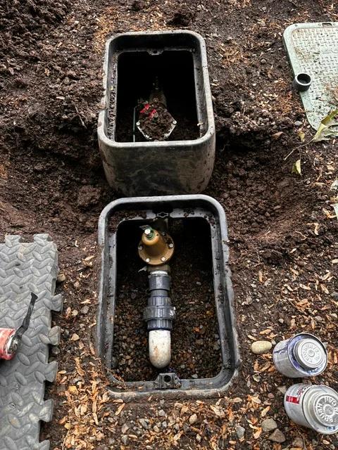 Two underground sprinkler valve boxes with brass irrigation valve and control stem visible