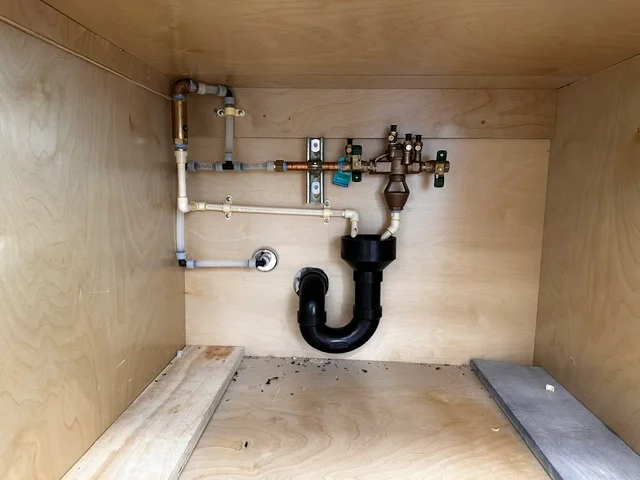 Under-sink plumbing with PVC pipes, shut-off valves, and P-trap drain assembly installed in cabinet