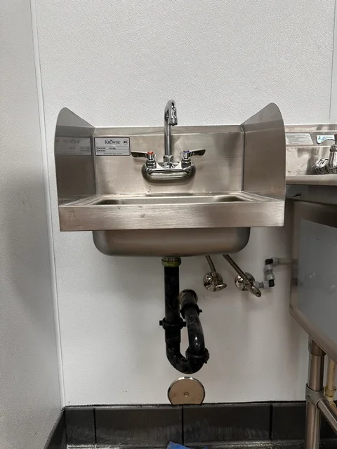 Stainless steel commercial sink with dual splash guards and chrome faucet mounted on white wall
