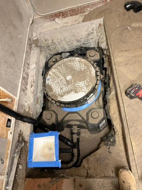 Sump pump installation in basement pit with blue discharge line and protective covering