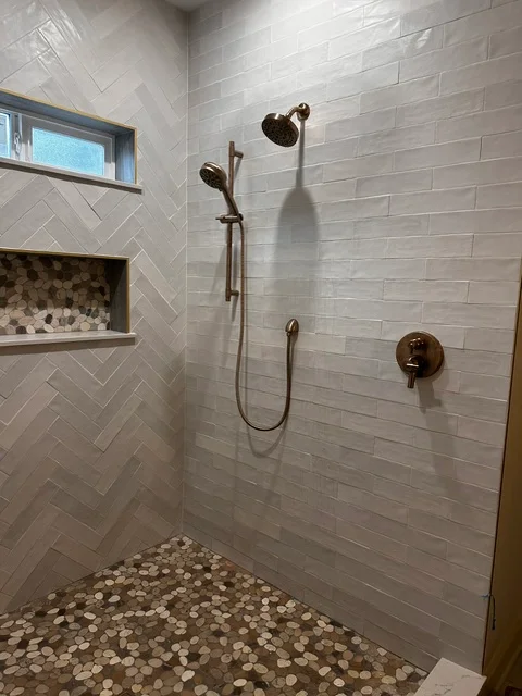 Modern bathroom shower with white subway tile walls, bronze fixtures, and pebble stone floor