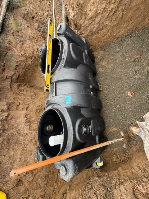 Black PVC sewer pipe installed in excavated trench with measurement tools
