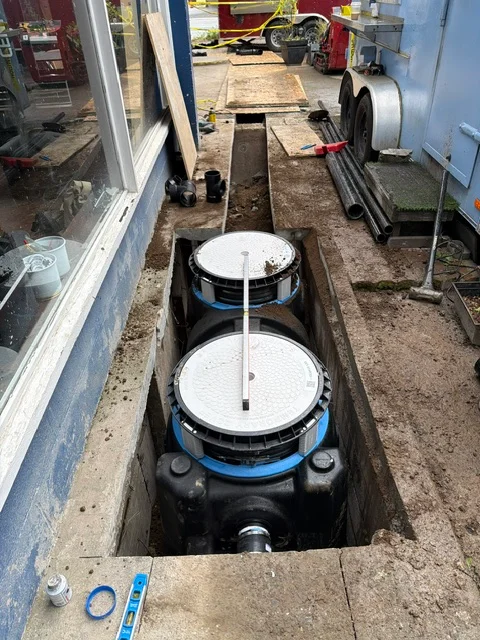 Dual septic tanks installed in ground excavation with white covers and blue bands