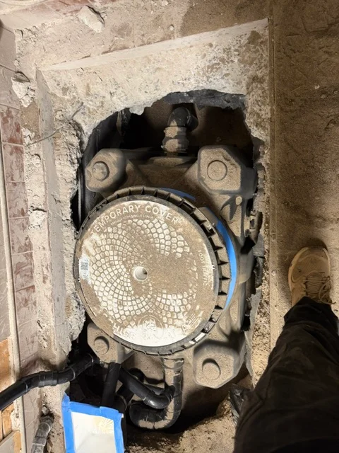 New sewer cleanout cover installed in concrete foundation with blue marking tape